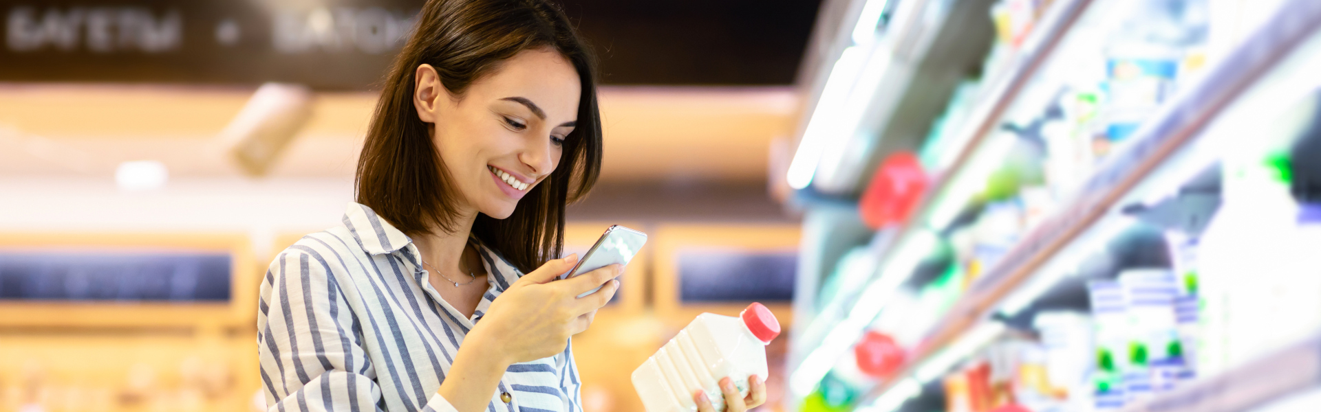 Junge Frau scannt mit ihrem Smartphone ein Produkt im Supermarkt und lächelt dabei