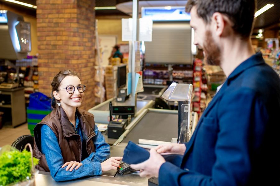 Kassiererin lächelt einen Geschäftsmann an der Kasse eines Supermarkts an